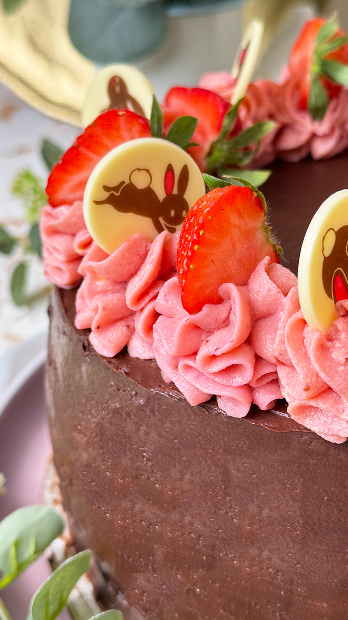 Erdbeer-Schokoladen-Torte mit Schokoglasur, Erdbeercreme und Deko, ein Stück ist angeschnitten und liegt auf einem Teller.