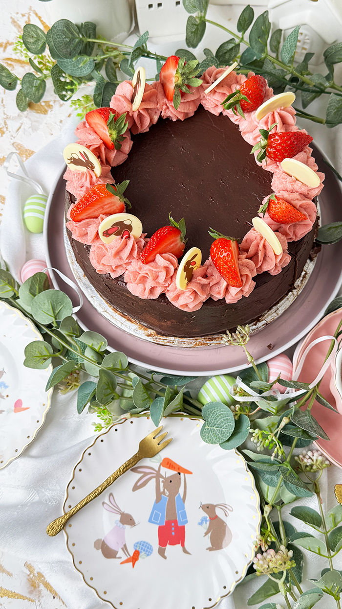 Erdbeer-Schokoladen-Torte mit Schokoglasur, Erdbeercreme und Deko, ein Stück ist angeschnitten und liegt auf einem Teller.