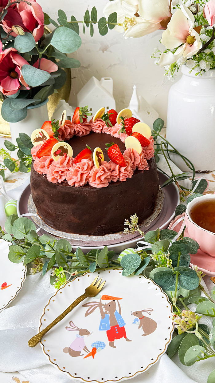Erdbeer-Schokoladen-Torte mit Schokoglasur, Erdbeercreme und Deko, ein Stück ist angeschnitten und liegt auf einem Teller.