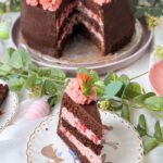 Erdbeer-Schokoladen-Torte mit Schokoglasur, Erdbeercreme und Deko, ein Stück ist angeschnitten und liegt auf einem Teller.