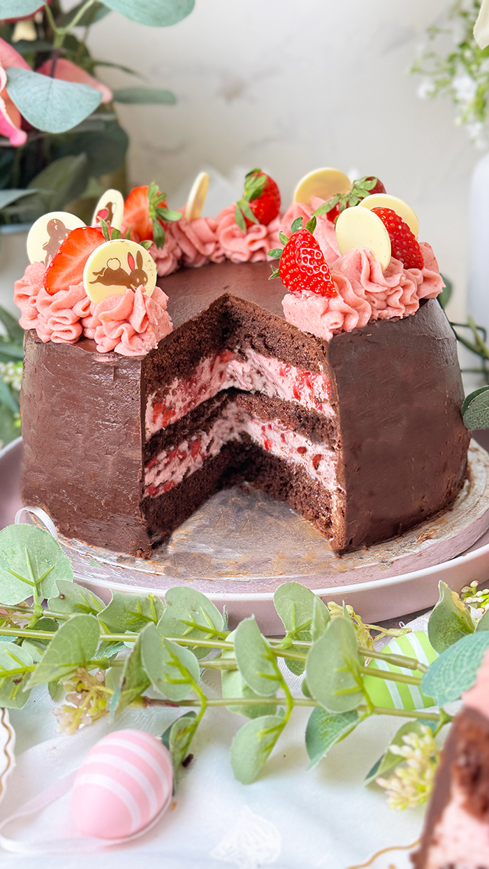 Erdbeer-Schokoladen-Torte mit Schokoglasur, Erdbeercreme und Deko, ein Stück ist angeschnitten und liegt auf einem Teller.
