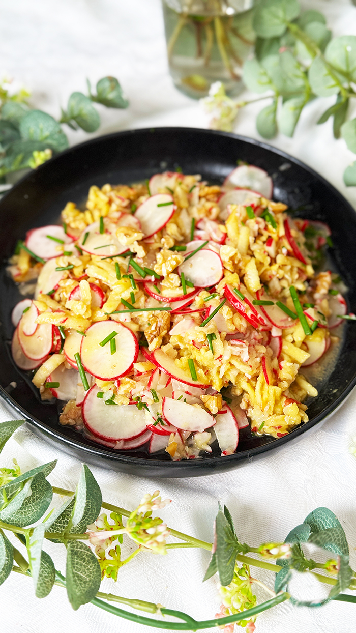 Radieschensalat mit Apfel und Walnüssen auf einen schwarzen Teller