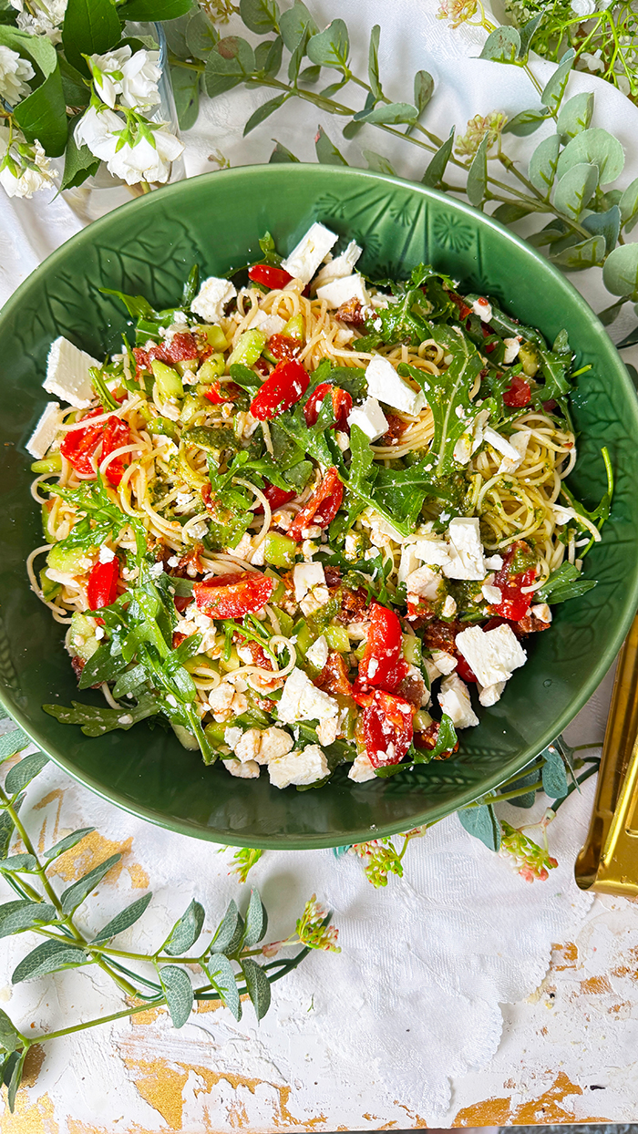 Leichter und aromatischer Spaghettisalat mit cremigem Feta, würzigem Pesto, frischen Tomaten und Rucola in einer Schüssel