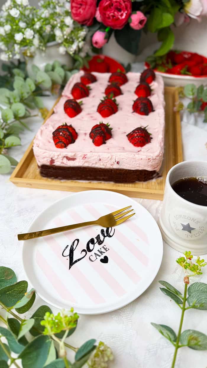 Ein Erdbeeren-Schoko-Kuchen vom Blech mit cremiger Erdbeer-Joghurt-Sahne und frischen Erdbeeren auf einem saftigen Schokobiskuitboden, dekoriert mit Schoko-Erdbeeren goldener Gabel.