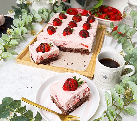 Erdbeeren-Schoko-Kuchen vom Blech mit cremiger Erdbeer-Joghurt-Sahne und frischen Erdbeeren auf einem saftigen Schokobiskuitboden, dekoriert mit Schoko-Erdbeeren und serviert auf einem Teller mit goldener Gabel.