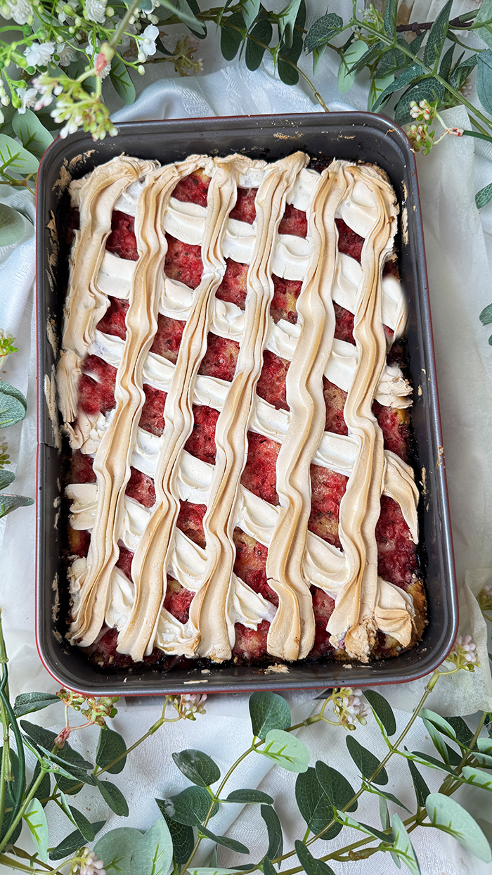 Johannisbeerkuchen mit Baiser vom Blech, in Stücke geschnitten, mit frischen Beeren und Kaffee serviert.