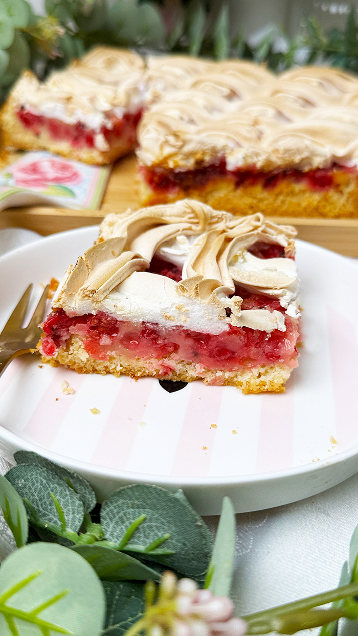 Johannisbeerkuchen mit Baiser vom Blech, in Stücke geschnitten, mit frischen Beeren und Kaffee serviert.
