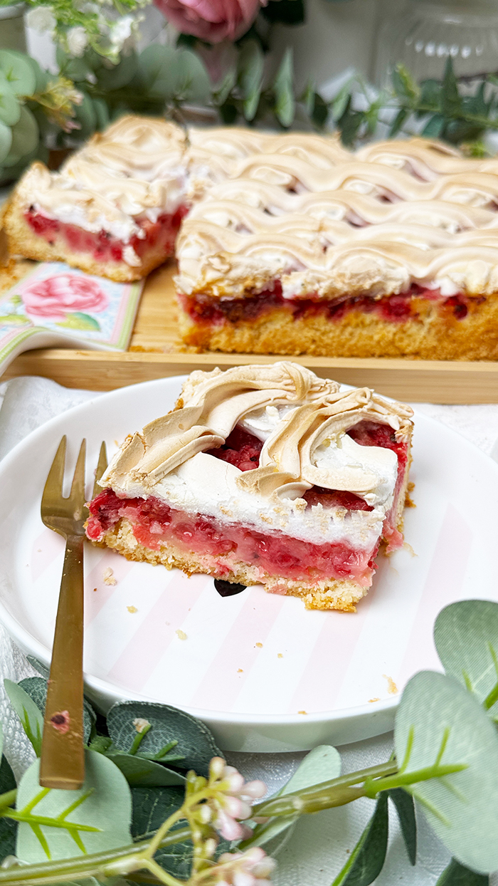 Johannisbeerkuchen mit Baiser vom Blech, in Stücke geschnitten, mit frischen Beeren und Kaffee serviert.