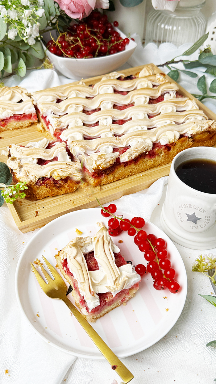 Johannisbeerkuchen mit Baiser vom Blech, in Stücke geschnitten, mit frischen Beeren und Kaffee serviert.