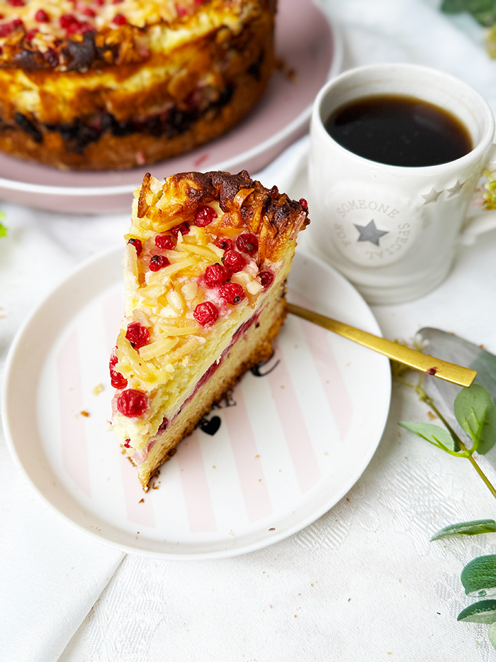 Ein Stück Johannisbeerkuchen mit Mascarponecreme und goldbraunem Mandel-Crunch auf einem Teller, ein Kuchen mit Mandeln und Johannisbeeren