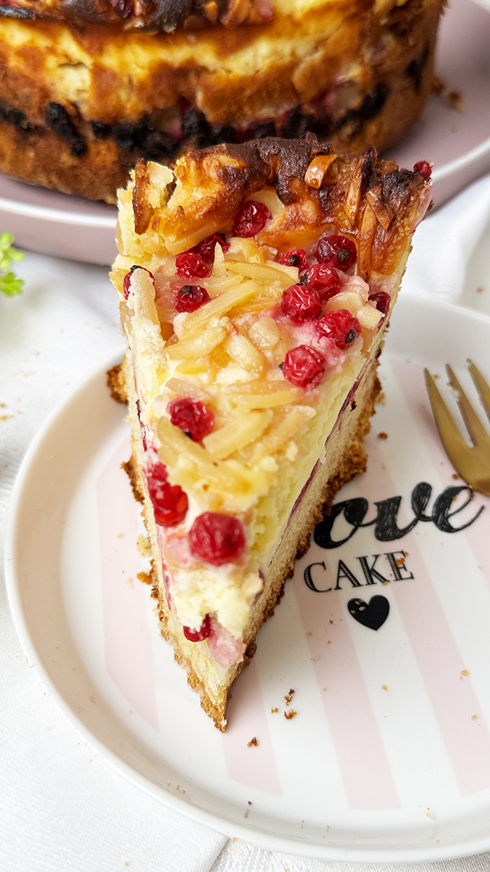 Ein Stück Johannisbeerkuchen mit Mascarponecreme und goldbraunem Mandel-Crunch auf einem Teller, ein Kuchen mit Mandeln und Johannisbeeren