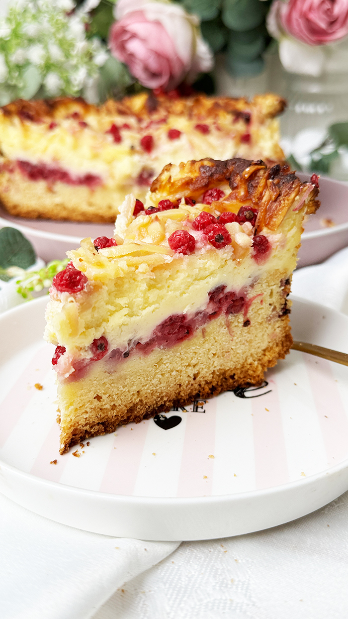 Ein Stück Johannisbeerkuchen mit Mascarponecreme und goldbraunem Mandel-Crunch auf einem Teller, ein Kuchen mit Mandeln und Johannisbeeren