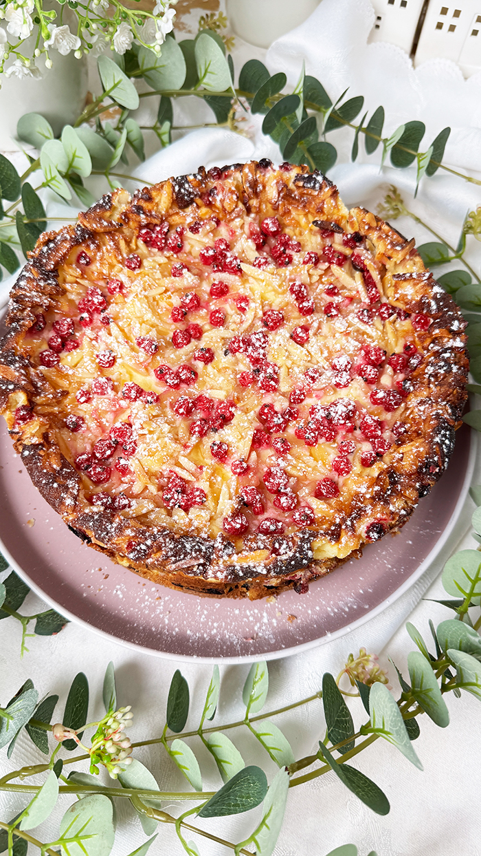 Ein Johannisbeerkuchen mit Mascarponecreme und goldbraunem Mandel-Crunch auf einem Teller, ein Kuchen mit Mandeln und Johannisbeeren