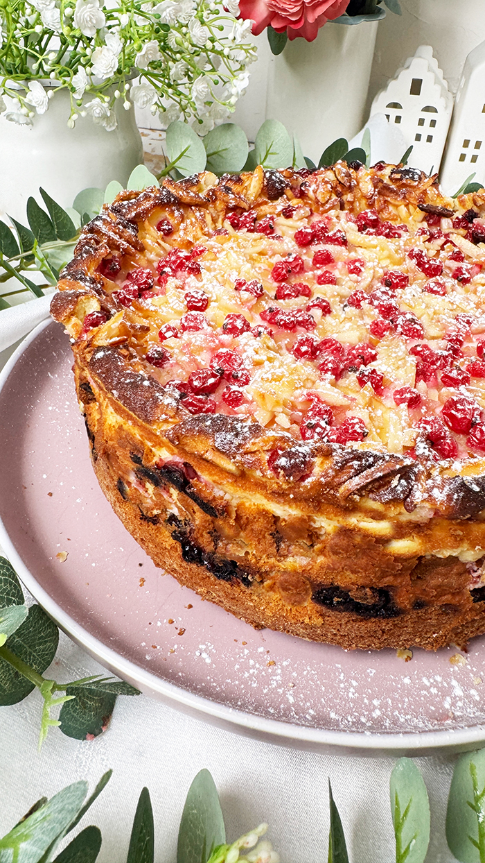 Ein Johannisbeerkuchen mit Mascarponecreme und goldbraunem Mandel-Crunch auf einem Teller, ein Kuchen mit Mandeln und Johannisbeeren
