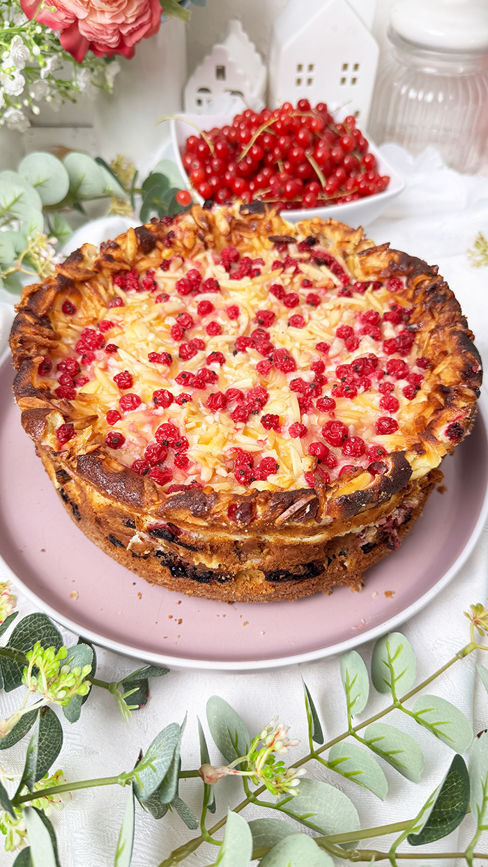 Ein Johannisbeerkuchen mit Mascarponecreme und goldbraunem Mandel-Crunch auf einem Teller, ein Kuchen mit Mandeln und Johannisbeeren
