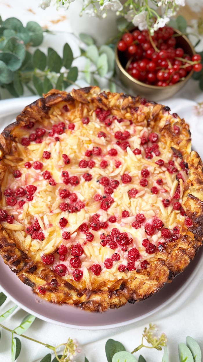 Ein Johannisbeerkuchen mit Mascarponecreme und goldbraunem Mandel-Crunch auf einem Teller, ein Kuchen mit Mandeln und Johannisbeeren