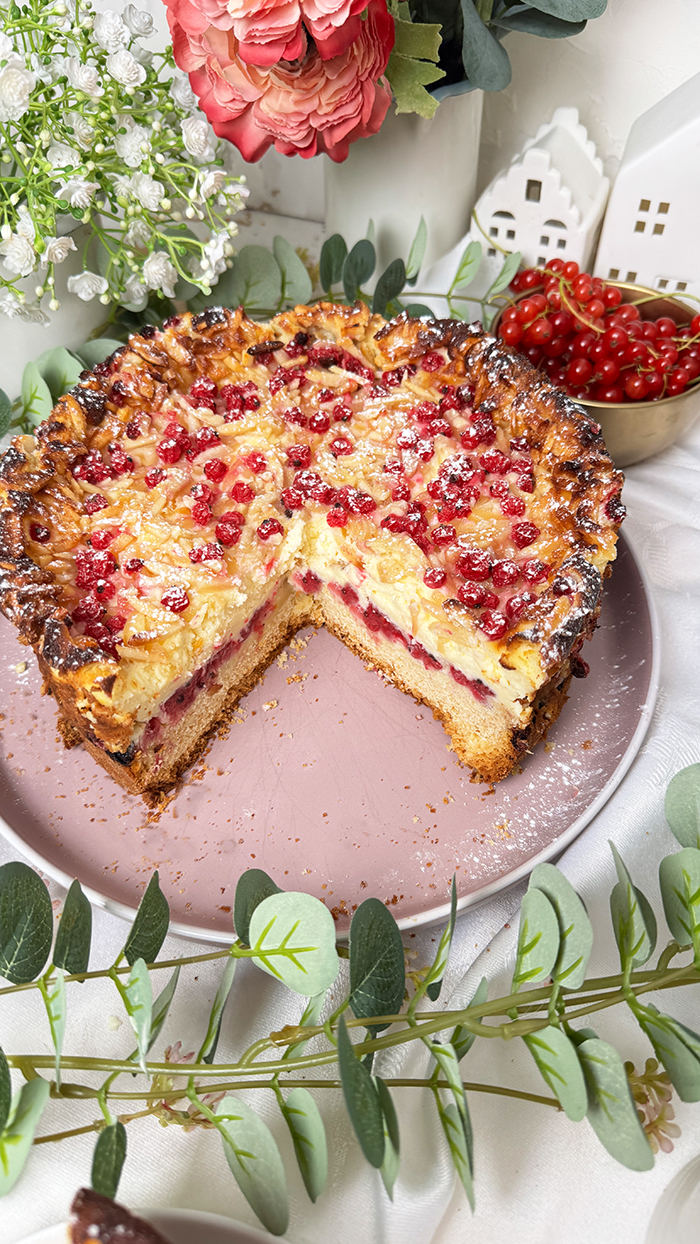 Ein Johannisbeerkuchen mit Mascarponecreme und goldbraunem Mandel-Crunch auf einem Teller, ein Kuchen mit Mandeln und Johannisbeeren