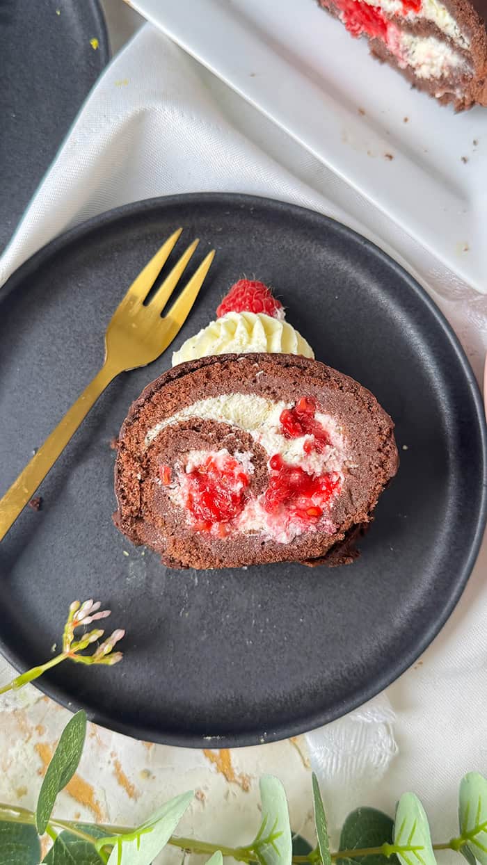 Schoko-Biskuitrolle mit Himbeeren und Sahnefüllung und frischen Himbeeren, dekoriert mit Sahnetuffs und Himbeeren, serviert mit Kaffee