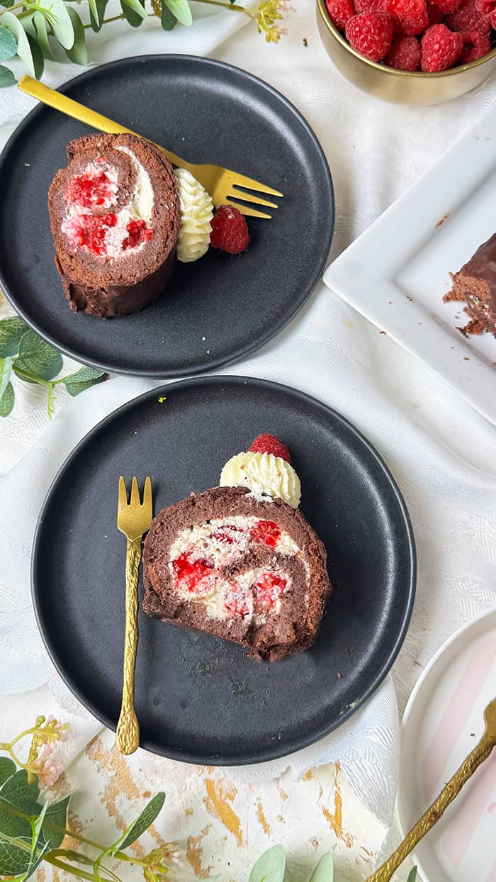 Schoko-Biskuitrolle mit Himbeeren und Sahnefüllung und frischen Himbeeren, dekoriert mit Sahnetuffs und Himbeeren, serviert mit Kaffee