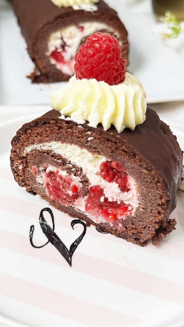 Schoko-Biskuitrolle mit Himbeeren und Sahnefüllung und frischen Himbeeren, dekoriert mit Sahnetuffs und Himbeeren, serviert mit Kaffee