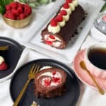 Schoko-Biskuitrolle mit Sahnefüllung und frischen Himbeeren, dekoriert mit Sahnetuffs und Himbeeren, serviert mit Kaffee