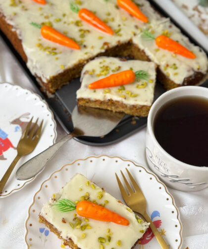 Schweizer Rüblikuchen: Das Original-Rezept für den einfachen saftigen Klassiker 1 Saftiges Stück Schweizer Rüblikuchen mit weißem Zuckerguss, Pistazien und einer Marzipanrübe auf einem weißen Teller mit Goldrand