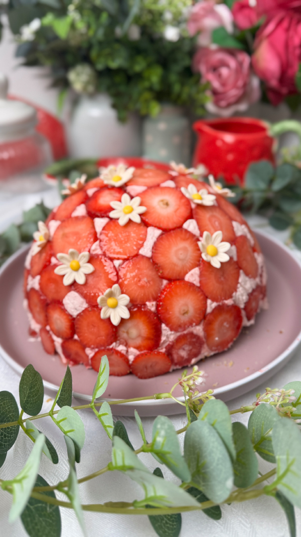 Erdbeer-Kuppeltorte – cremig, fruchtig & unwiderstehlich 1 Erdbeer-Kuppeltorte mit zartem Erdbeermuster außen auf einer Tortenplatte, dekoriert mit Dekorblüten