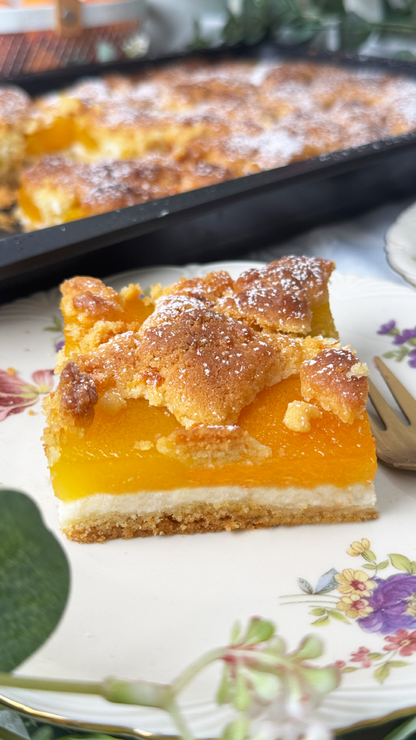 Österreichischer Marillen-Streuselkuchen vom Blech - Omas bestes Rezept 3 Österreichischer Marillenkuchen vom Blech mit saftigen Aprikosen auf einem gedeckten Kaffeetisch, serviert mit einer Tasse Tee und einem angeschnittenen Kuchenstück auf Vintage-Geschirr.
Bildbeschreibung