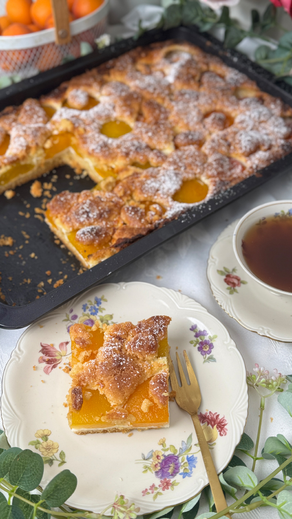 Österreichischer Marillen-Streuselkuchen vom Blech - Omas bestes Rezept 1 Österreichischer Marillenkuchen vom Blech mit saftigen Aprikosen auf einem gedeckten Kaffeetisch, serviert mit einer Tasse Tee und einem angeschnittenen Kuchenstück auf Vintage-Geschirr.