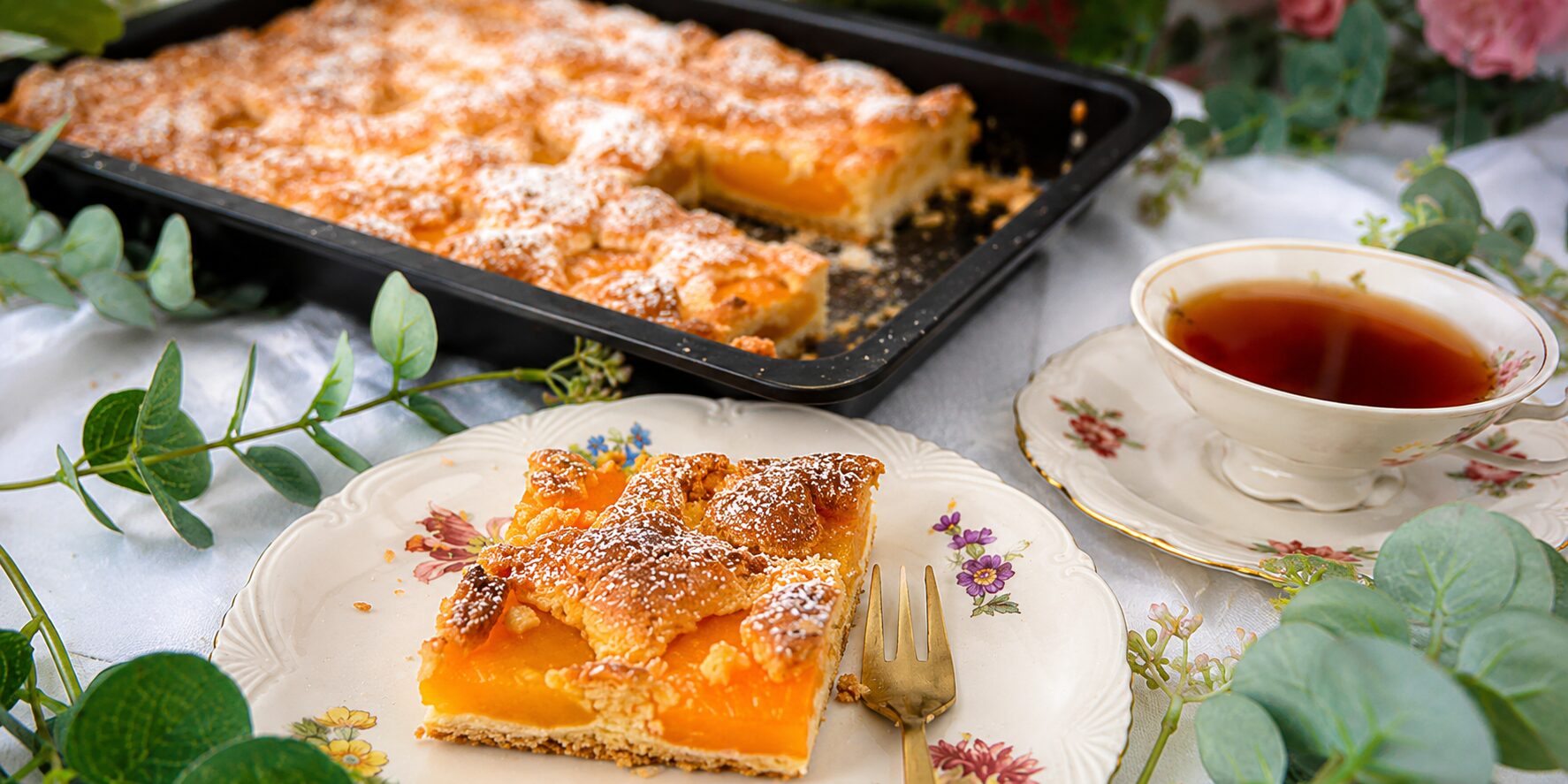 Österreichischer Marillen-Streuselkuchen vom Blech - Omas bestes Rezept 4 Österreichischer Marillen-Streuselkuchen vom Blech mit saftigen Aprikosen auf einem gedeckten Kaffeetisch, serviert mit einer Tasse Tee und einem angeschnittenen Kuchenstück auf Vintage-Geschirr. Bildbeschreibung
