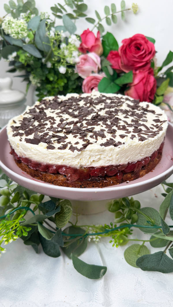 Stachelbeertorte mit Mascarpone, einfach fruchtig und cremig 2 Eine selbstgemachte Stachelbeertorte mit Mascarpone-Creme und Schokostreuseln auf einer rosa Etagere, im Hintergrund dekorative Blumen.