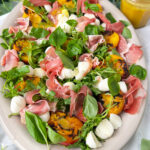 Gegrillter Nektarinensalat mit Rucola, Mini Mozzarella, Parmaschinken und Honig Zitronen Dressing auf einer Servierplatte.