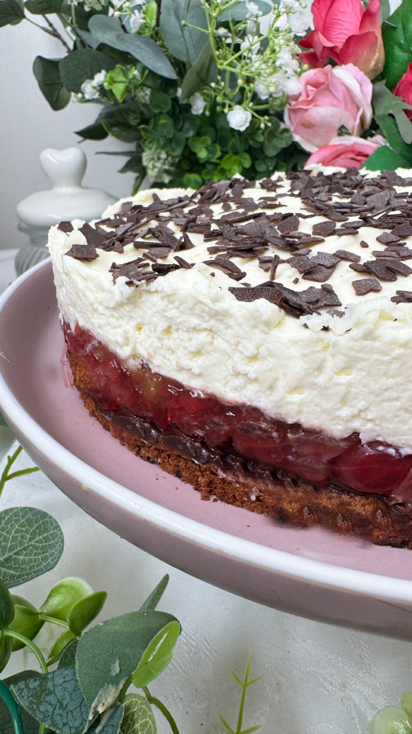 Stachelbeertorte mit Mascarpone, einfach fruchtig und cremig 3 Eine selbstgemachte Stachelbeertorte mit Mascarpone-Creme und Schokostreuseln auf einer rosa Etagere, im Hintergrund dekorative Blumen.