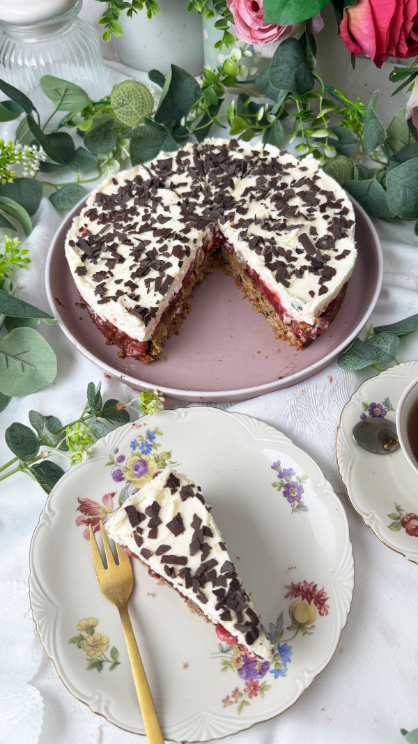 Stachelbeertorte mit Mascarpone, einfach fruchtig und cremig 6 Eine selbstgemachte Stachelbeertorte mit Mascarpone-Creme und Schokostreuseln auf einer rosa Etagere, im Hintergrund dekorative Blumen.