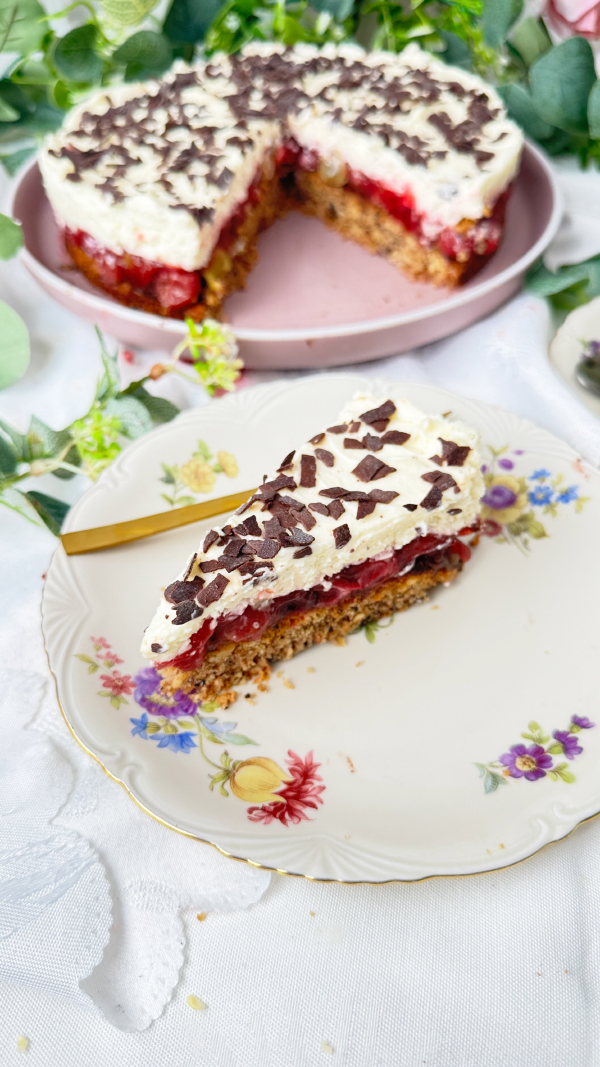 Stachelbeertorte mit Mascarpone, einfach fruchtig und cremig 1 Eine selbstgemachte Stachelbeertorte mit Mascarpone-Creme und Schokostreuseln auf einer rosa Etagere, im Hintergrund dekorative Blumen.