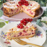 Johannisbeerkuchen mit Quark und Streuseln, angeschnitten mit einem Kuchenstück und frischen roten Johannisbeeren