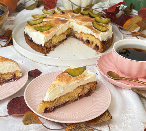 Angeschnittener Zwetschgen-Schmand-Kuchen mit saftigem Zwetschgenbelag und cremiger Schmandhaube, dazu ein Kuchenstück auf einem rosa Teller.