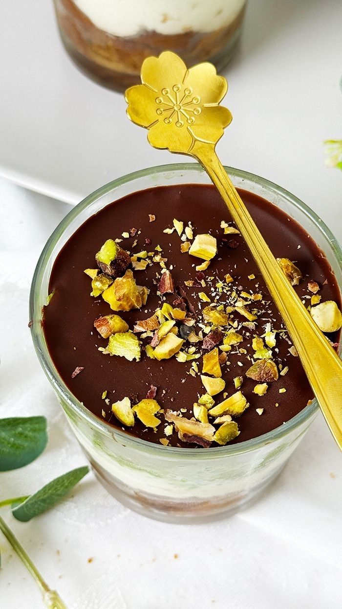 Ein kunstvoll Dubai Schokoladen Tiramisu geschichtetes Tiramisu im Glas, bestehend aus Schokoladenbiskuit, cremiger Mascarpone, Pistaziencreme und einer Schokoladenglasur, garniert mit gehackten Pistazien.