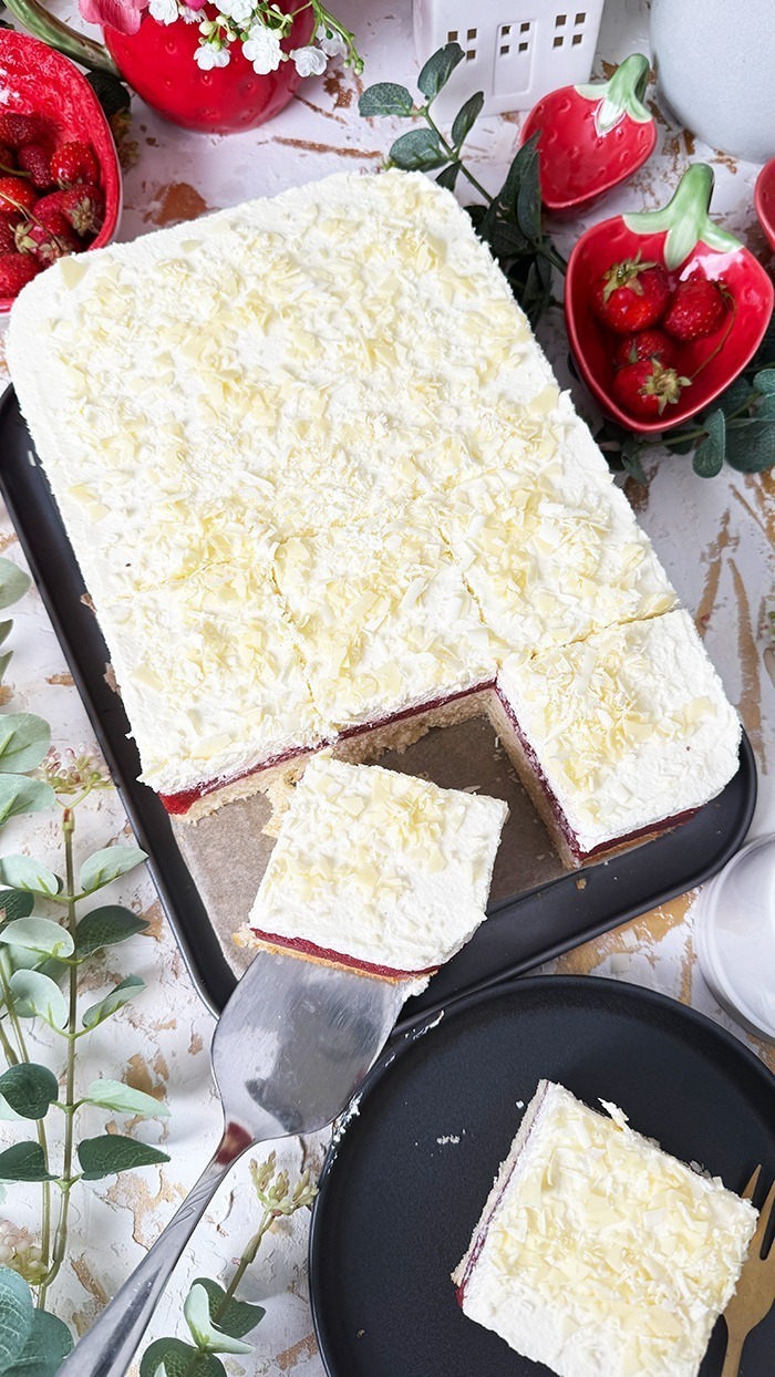 Das auf dem Bild gezeigte Kuchen ist ein "Frau Holle Kuchen". Er besteht aus mehreren Schichten: einem Biskuitboden, einer Erdbeer- oder Beerenschicht und einer cremigen oberen Schicht, die möglicherweise mit weißen Schokoladenraspeln garniert ist. Dieser Kuchen ist oft nach der Märchenfigur "Frau Holle" benannt und wird typischerweise mit frischen Zutaten zubereitet, wodurch eine köstliche Kombination aus Fruchtigkeit und Cremigkeit entsteht. 