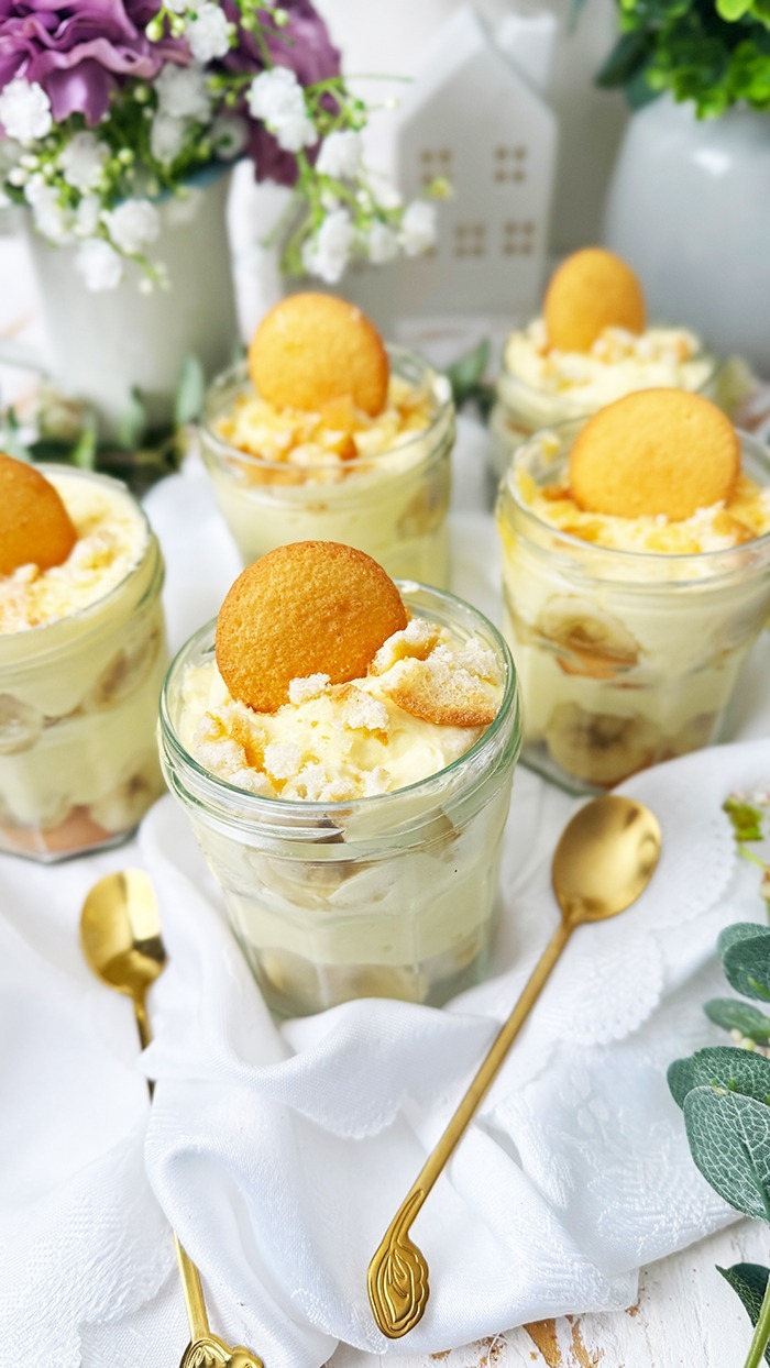 Das Bild zeigt mehrere Gläser, die mit dem berühmten Banana Pudding der Magnolia Bakery gefüllt sind. Jedes Glas ist in Schichten aufgebaut und enthält Vanillewaffeln, Bananenscheiben und cremigen Vanillepudding.
