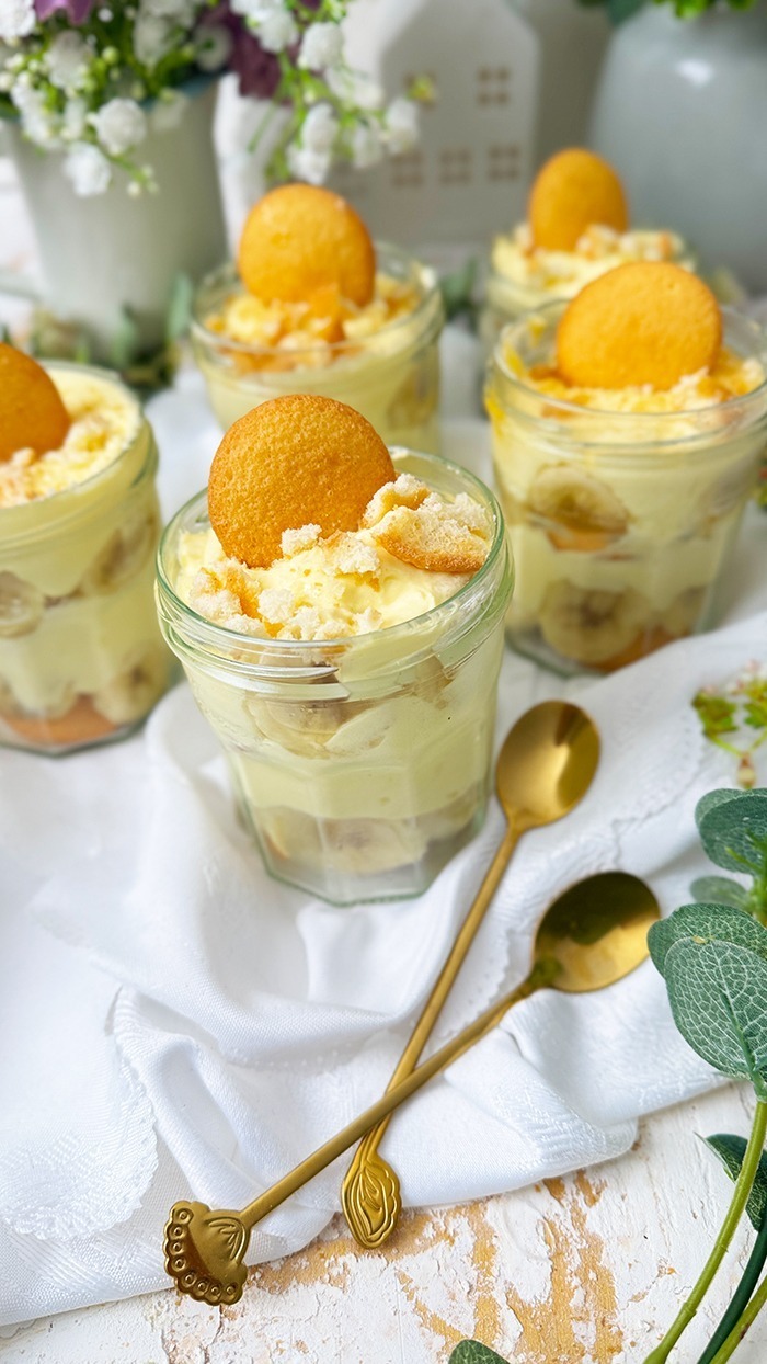 Das Bild zeigt mehrere Gläser, die mit dem berühmten Banana Pudding der Magnolia Bakery gefüllt sind. Jedes Glas ist in Schichten aufgebaut und enthält Vanillewaffeln, Bananenscheiben und cremigen Vanillepudding.