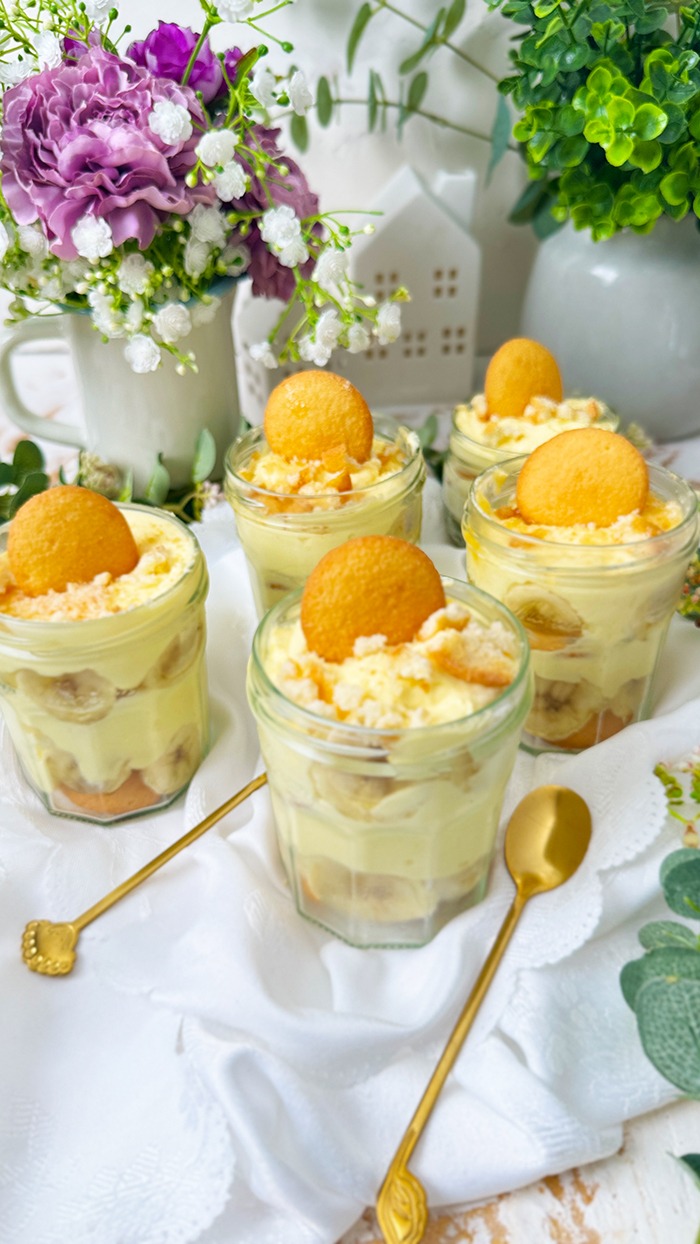 Das Bild zeigt mehrere Gläser, die mit dem berühmten Banana Pudding der Magnolia Bakery gefüllt sind. Jedes Glas ist in Schichten aufgebaut und enthält Vanillewaffeln, Bananenscheiben und cremigen Vanillepudding.