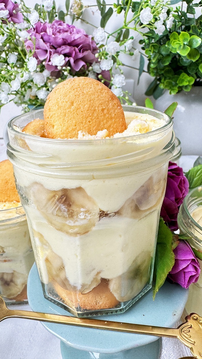 Das Bild zeigt mehrere Gläser, die mit dem berühmten Banana Pudding der Magnolia Bakery gefüllt sind. Jedes Glas ist in Schichten aufgebaut und enthält Vanillewaffeln, Bananenscheiben und cremigen Vanillepudding.