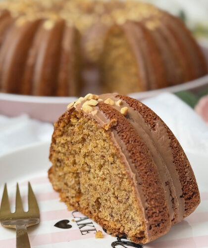 Ein saftiger Nusskuchen im Gugelhupf-Stil mit Haselnussglasur und gehackten Nüssen liegt auf einem dekorativen Teller, während der gesamte Kuchen im Hintergrund präsentiert wird.
